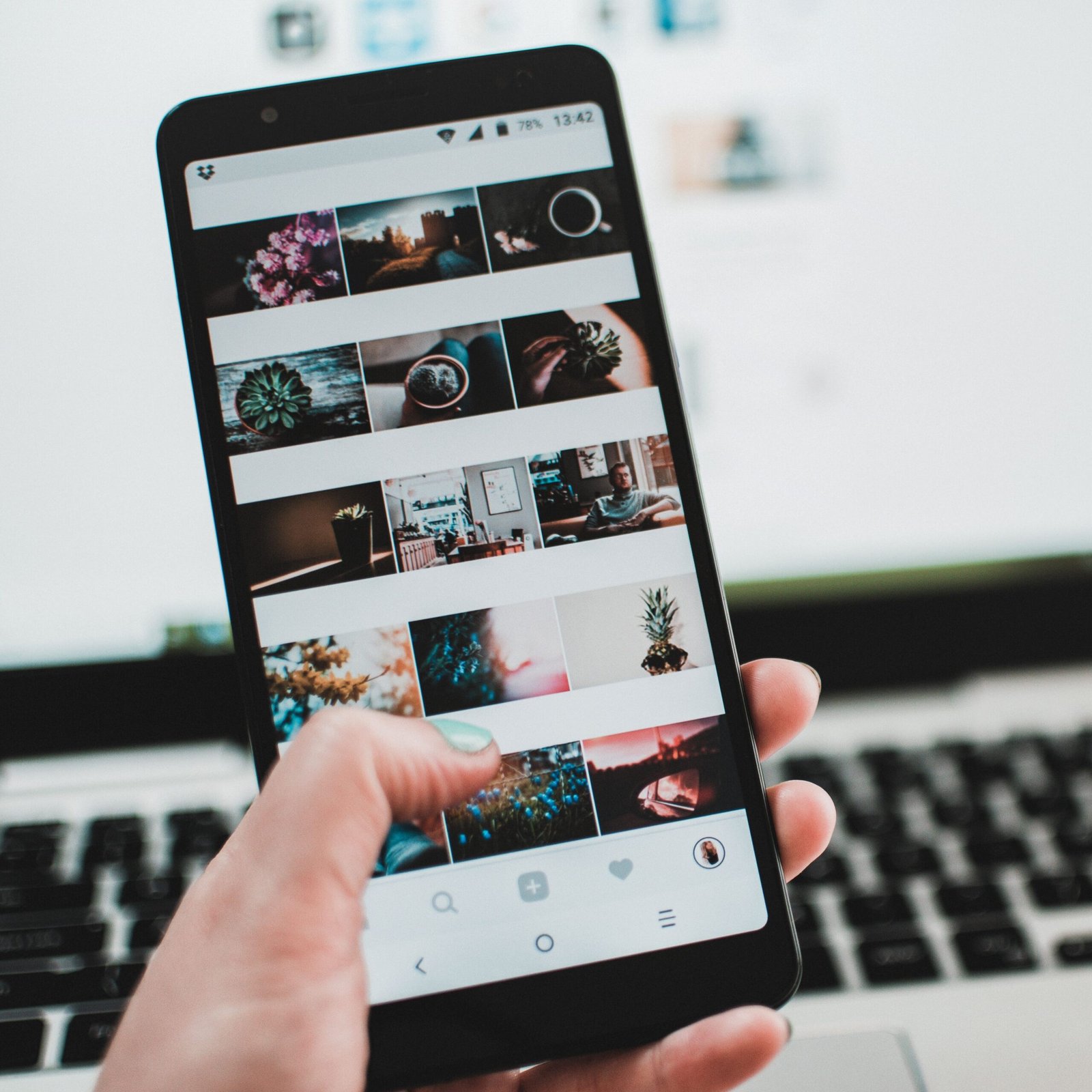 A person uses a smartphone to browse social media in front of a laptop, emphasizing modern technology and lifestyle.