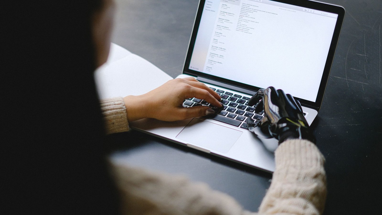 A person with a prosthetic hand using a laptop, showcasing technology and inclusivity.